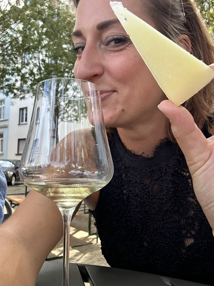 Hannah hält ein Stück Bergkäse neben ein Glas Weißwein