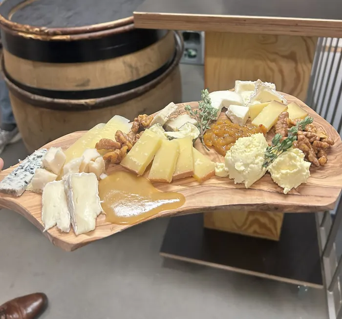 Holzbrett mit Käse, Nüssen, Chutney und Kräutern auf einem Weinfass