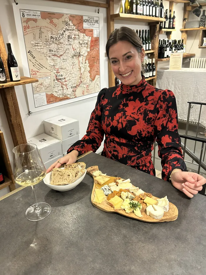 Hannah lächelt an einem Tisch mit Käseplatte, Brot und einem Glas Weißwein